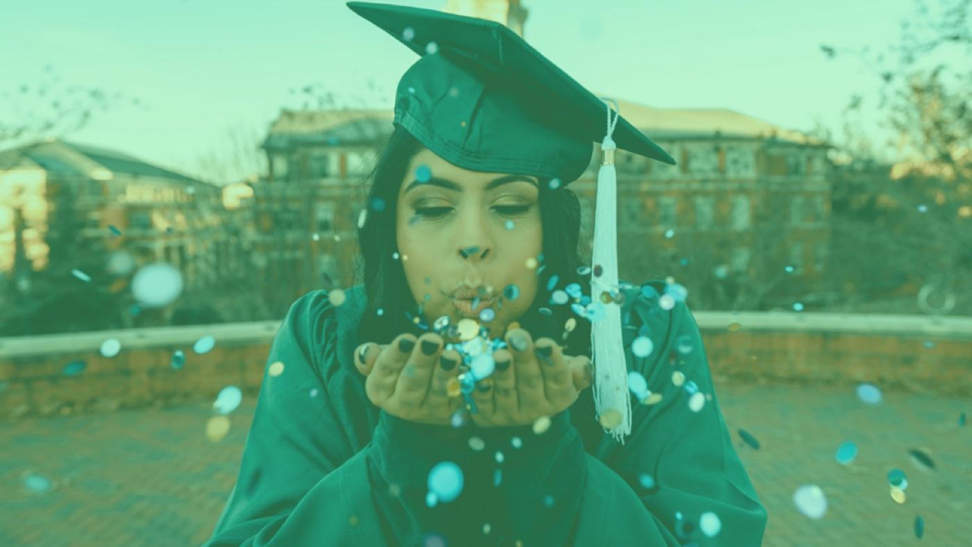 A graduate in cap and gown blowing confetti